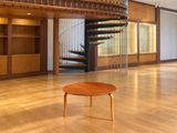 une table en bois au milieu d'une pièce, avec un escalier en colimaçon en arrière-plan