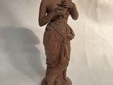 une statue représentant une femme tenant un oiseau, sur fond blanc