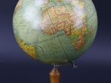 un globe vert posé sur un socle en bois, sur fond noir