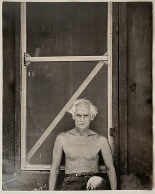 black and white photograph of an old man sitting in front of a window