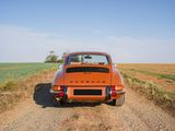 an orange car parked on a dirt road in the middle of a field