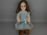 une vieille poupée vêtue d'une robe bleue et de chaussures marron, assise sur une surface grise