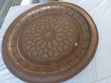 une grande assiette en cuivre posée sur une table recouverte d'une nappe blanche