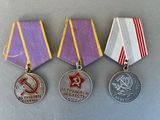 three medals are displayed on a gray surface with a red star and hammer