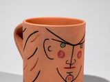 un gobelet orange sur lequel est dessiné le visage d'une femme