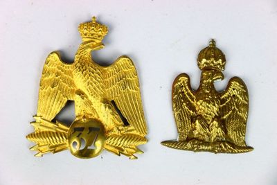 deux insignes représentant un aigle doré sur fond blanc, l'un surmonté d'une couronne et l'autre surmonté d'une couronne
