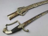 pair of silver plated swords on a white surface
