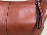 brown leather purse with zippers on top of it on a white surface
