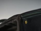 the back of a black purse with a gold button on it