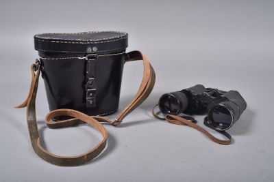 un sac noir muni d'une bandoulière marron, avec une paire de jumelles posée à côté
