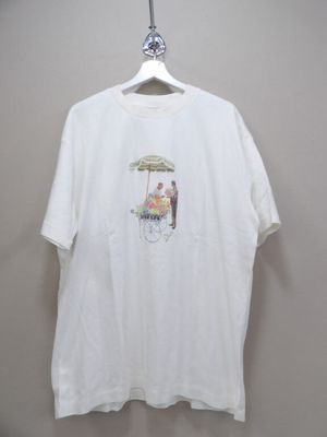 white t - shirt with a picture of a man sitting in a chair under an umbrella on a hanger