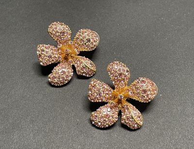 two gold tone flower earrings with pink crystals on a black surface