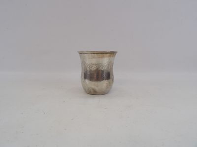 une tasse en argent posée sur une surface blanche, avec un mur blanc en arrière-plan