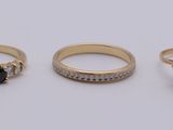 trois bagues en or ornées de diamants noirs et blancs, posées sur un fond blanc