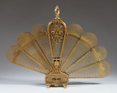 un éventail plaqué or richement décoré, surmonté d'un oiseau