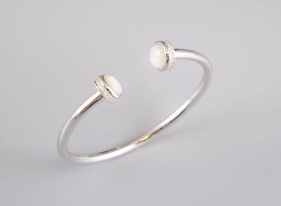 a silver cuff bracelet with two white pearls on a white background