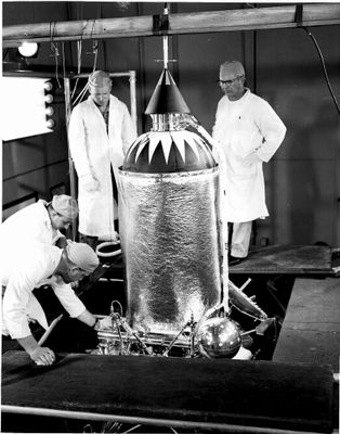 photo en noir et blanc de trois hommes en blouse de laboratoire travaillant sur un grand objet