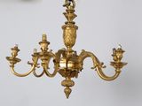 a gold chandelier hanging from a ceiling with a clock on the wall