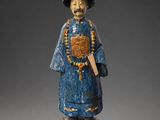 une vieille statue en bois représentant un homme coiffé d'un chapeau et muni d'une canne