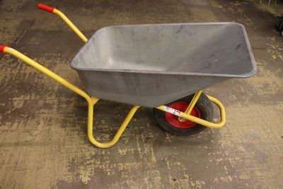 une brouette jaune avec une poignée rouge posée par terre