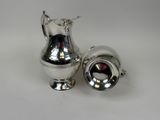 a silver pitcher and a silver cup on a white table