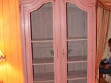 a pink cabinet in the corner of a room with a chandelier in the background