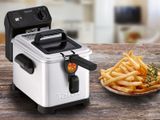 an electric deep fryer sitting on top of a wooden table next to a plate of french fries