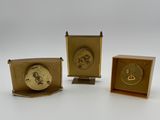 three small brass clocks sitting next to each other on a white surface