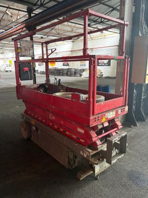 a red scissor sitting in a warehouse with a white car in the background
