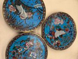 trois assiettes décoratives ornées d'oiseaux et de fleurs, posées sur une table
