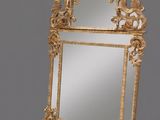 an ornately carved mirror with a gold frame on a grey background