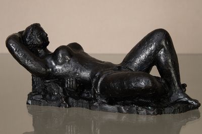 statue of a woman reclining on a rock on a glass table