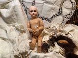 a baby doll sitting on a bed with a teddy bear