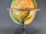 un vieux globe terrestre posé sur un socle en bois, sur fond gris