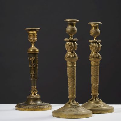 trois bougeoirs en laiton vieilli posés sur une table blanche, sur fond noir