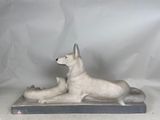 statue of a dog laying down on a pillow on a white background