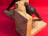 deux oiseaux noirs posés sur un serre-livres en bois, sur fond rouge
