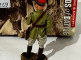 figurine of a man in a green uniform with a red hat and a red beret standing in front of a box