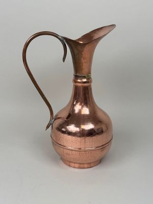 an antique copper pitcher with a curved handle on a white background