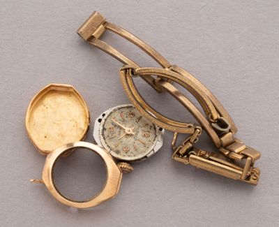 a gold watch and a gold tie bar on a gray surface