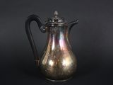 an antique silver coffee pot with a black handle on a black background