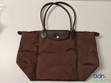Le sac Longchamp est marron et possède une poignée noire.