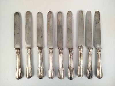 six silverplated knives are lined up on a white surface