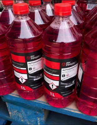 Plusieurs grandes bouteilles contenant un liquide rouge sont posées sur une étagère dans un magasin.