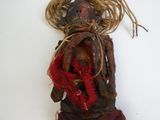 poupée vaudou avec des dreadlocks et un foulard rouge posée sur une surface blanche