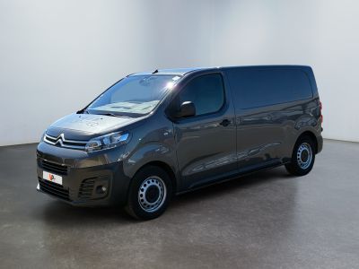 La camionnette grise est garée dans une grande pièce aux murs blancs.