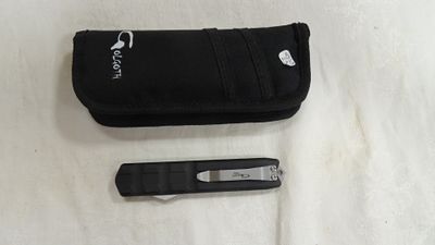 un portefeuille noir et un couteau posés sur une surface blanche