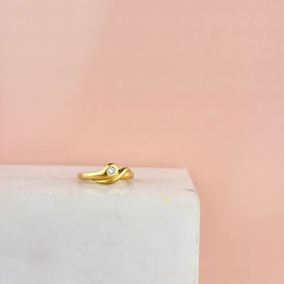 une bague en or sertie d'un diamant, posée sur un bloc de marbre blanc