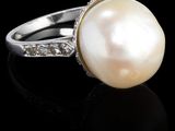 une photo d'une bague en perle et diamant posée sur un fond noir