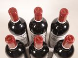 six bottles of red wine are lined up on a white surface
